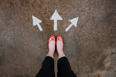 woman's legs and feet with red shoes on standing in front of an arrow on the ground that points in 3 directions