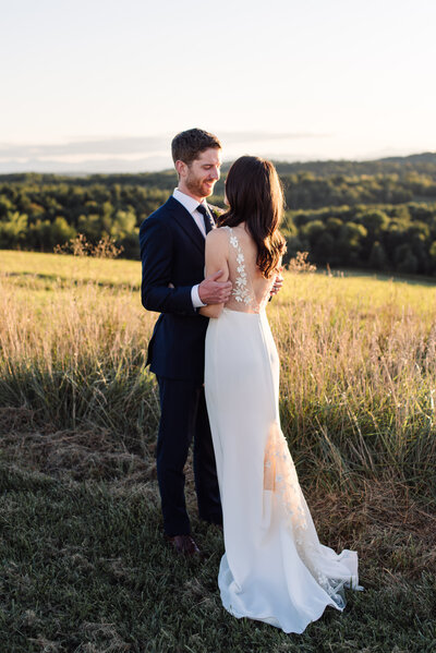 Bride and groom embrace on golden hillside in Vermont at Maquam Barn and winery