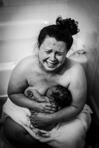 Mom is stiing on the bathroom floor after just having a very fast home birth. She is holding her baby and crying.