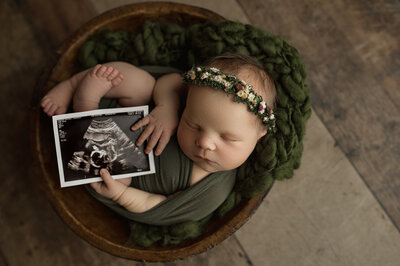 baby in green holding ultrasound photo
