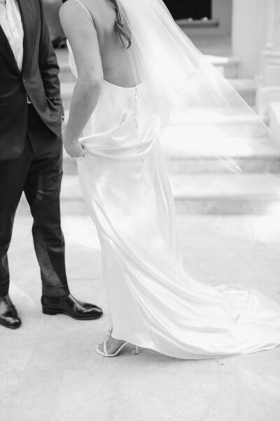 black and white image of bride and groom standing together with wind blowing bride's dress
