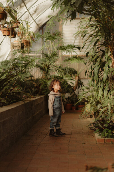 Little boy in sweater and denim overalls in a tropical greenhouse by Atlanta Children's Photographer