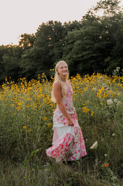 Teenage girl poses for the camera outside standing in an open field with wildflowers in her hands.