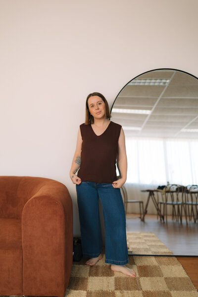 Liv Rollings standing by tall mirror and rust colored couch
