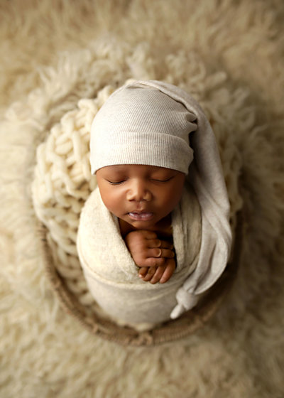 black newborn in neutral toned wrap with matching hat in basket on fur blanket