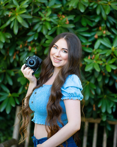 Mikayla Arsenian is a senior photographer and posing for a photo while holding a Nikon camera