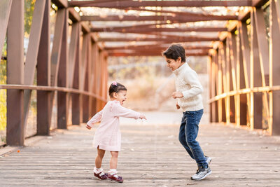 Young brother and sister chasing each other around on a cute bridge