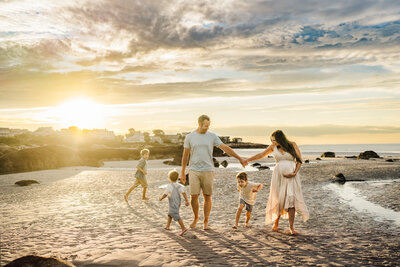 family with three boys runs on beach