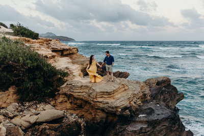 man & woman walking on cliff next to ocean