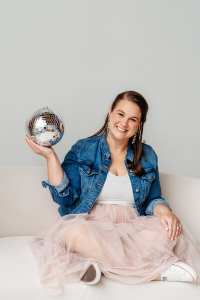 Female in jean jacket and light pink skirt kicking leg up on a couch.