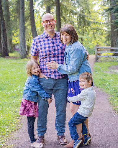 Two parents embrace as their two children hug and hang on their legs with one child hanging on each parent in Shoreline, Wa captured by Seattle Family Photographer, Becky Langseth.