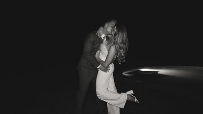 Couple in a black suit and white jumpsuit with heels kissing in the dark