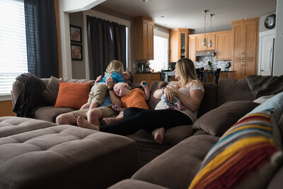 Documentary style photo of family boys playing on couch with dad while mom nurses baby
