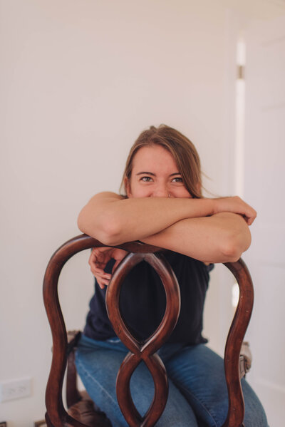 Marisa of Msav Creative Co sits in a backwards chair and crosses her arms while looking at the camera