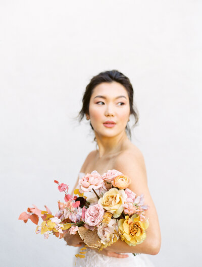 asian bride holding her pastel bouquet and looking off into the distance