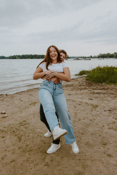 Husband lifting wife on a beach to celebrate saying their engagement in MN