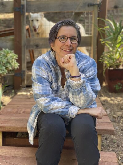 Woman sitting outside in front of greenery smiling