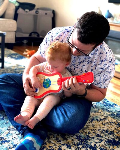 Scott holding Maddie playing toy guitar