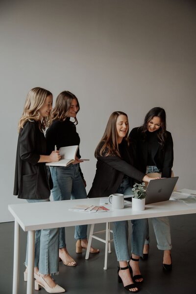 Four women looking over a desk together at a laptop