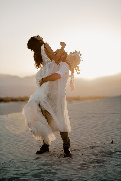 groom lifts bride in sand