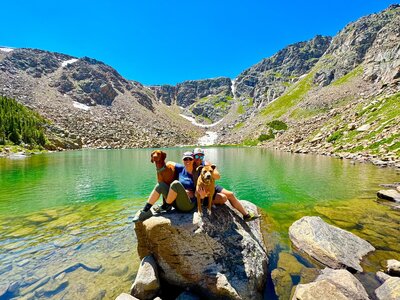couple with dogs on rock near mountain lake
