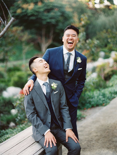 two grooms in suits laughing on their wedding day for portraits at the Japanese friendship garden in San Diego