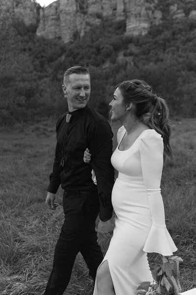 A bride and groom walk together through the grass looking at one another. They're taking bridal portraits in Eastern Idaho.