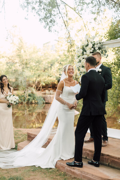 Bride laughing and crying at ceremony as groom gives his vows captured by a Scottsdale wedding photographer in a scenic outdoor wedding venue.