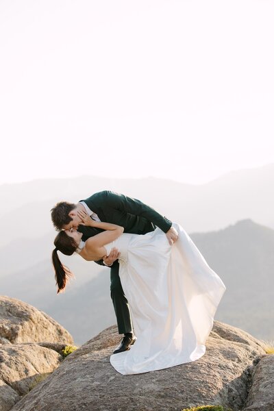 Stunning mountain wedding portrait with the bride and groom kissing on top of the mountain during golden hour in the rocky mountains