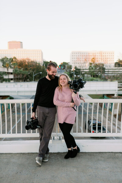 couple on bridge overlooking city with cameras in their hands