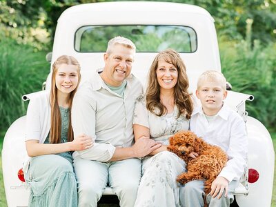 Family smiling and sitting in a truck together outdoors.