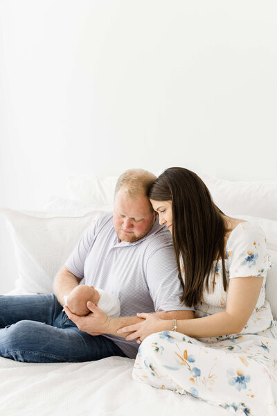 Dothan Alabama Mom and Dad sitting on a bed smiling looking at their baby during a newborn photography session