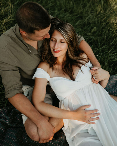 A pregnant couple, captured by a Pittsburgh family photographer, enjoying a serene moment on a blanket in the grass