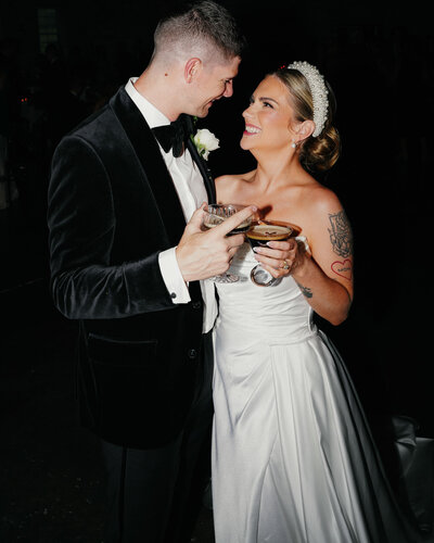 bride and groom are facing each other, smiling warmly and holding cocktails at grbic events wedding venue