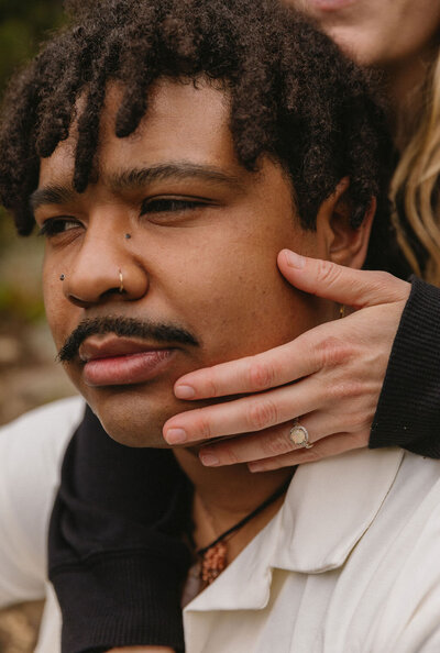 Editorial engagement photo of bride holding her ring hand delicately on her fiance's face