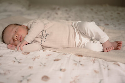 Newborn ligt op zijn zij te slapen met zijn voetjes over elkaar tijdens een newbornshoot