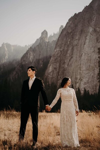 A bride and groom walking down a trail on the edge of the beach