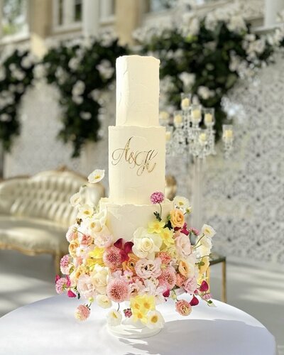 Three tier wedding cake in a Bridgerton style set up at Syon Park Conservatory - three tiers of textured buttercream with red and pink roses on a diagonal on the front of the cake with trailing foliage