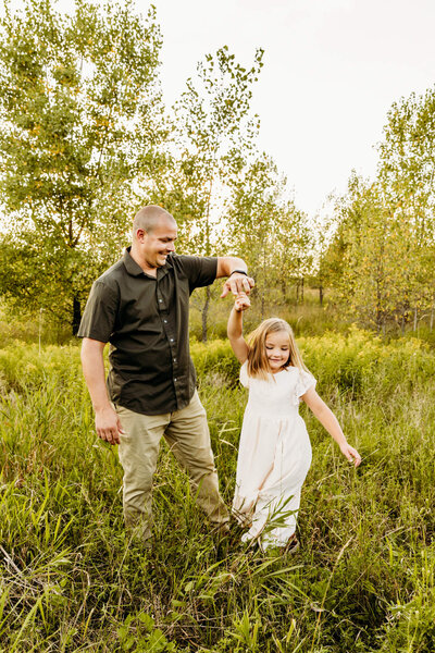 dad spinning his young daughter as they dance in a field captured by Ashley Kalbus Photography