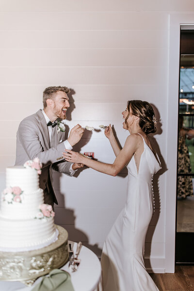 Bride and groom sharing a playful cake-cutting moment at their Westwynd Gardens wedding, photographed by Philadelphia wedding photographer Kayla Aspen.