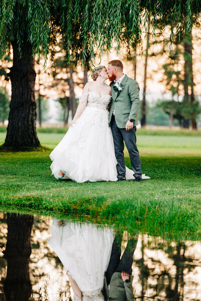 Bride and groom kissing by pond at The Barn at Finley Point in Polson, MT
