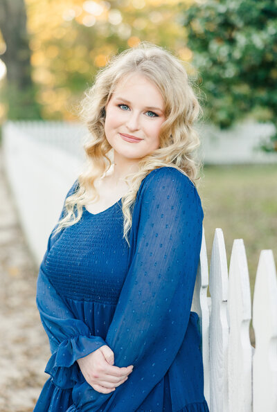 girl in a blue dress posing near a white picket fence