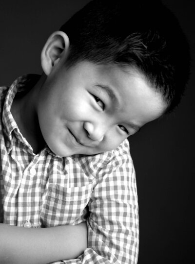 A black and white photo of a young boy smiling, with soft lighting highlighting his features.
