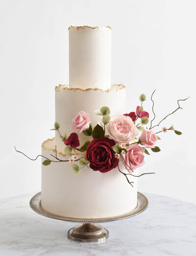 Three tiered white wedding cake with gold leaf edges and sugar flowers