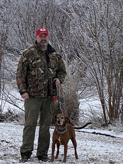 Man in Camo jacket standing n snow with dog