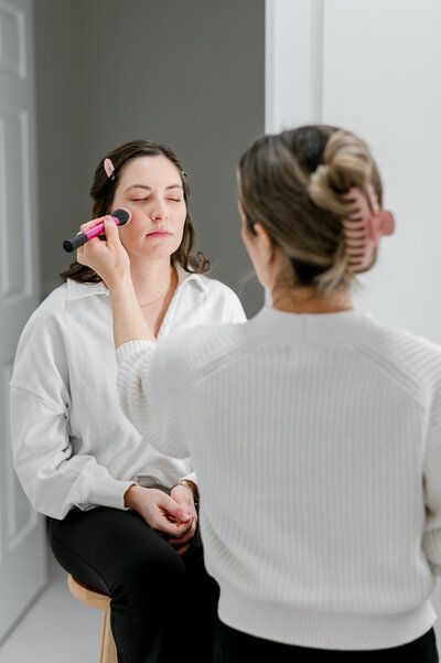 A client of Nashville newborn photographer Kristie Lloyd's sits on a stool while getting her makeup done before her photo session.