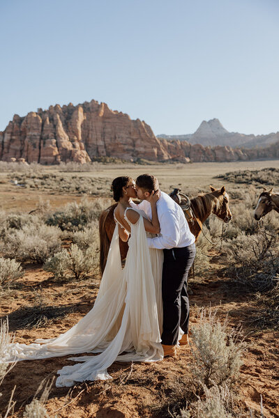 bride and groom kissing after saying vows in a utah desert with horses and mountains in background