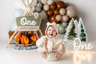 Happy baby boy sitting in front of balloons and a "one" sign.