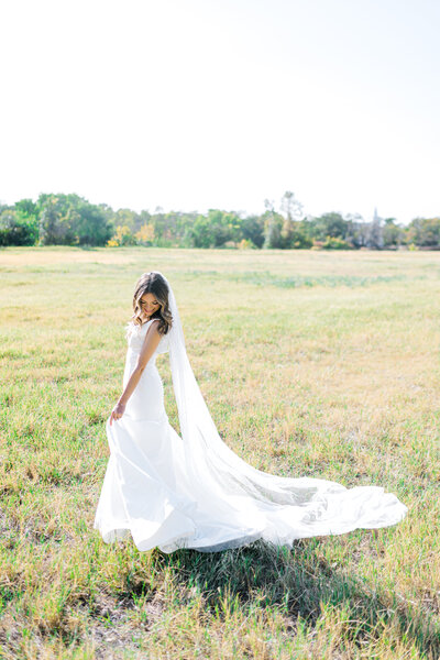 Portrait of a bride holding her dress while standing in a grassy field