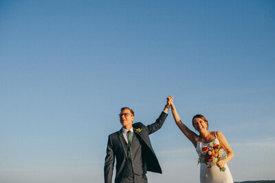 a wedding couple holds their hands in the air as they celebrate and smile